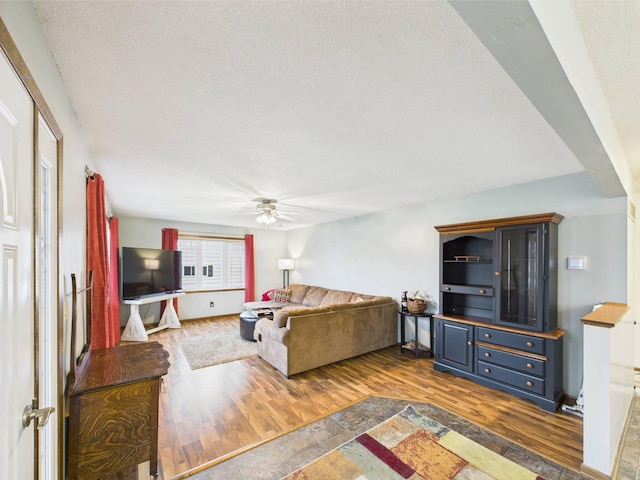 living area featuring baseboards, a ceiling fan, a textured ceiling, and dark wood-style floors