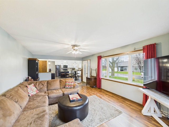 living area featuring baseboards, light wood-style flooring, and ceiling fan