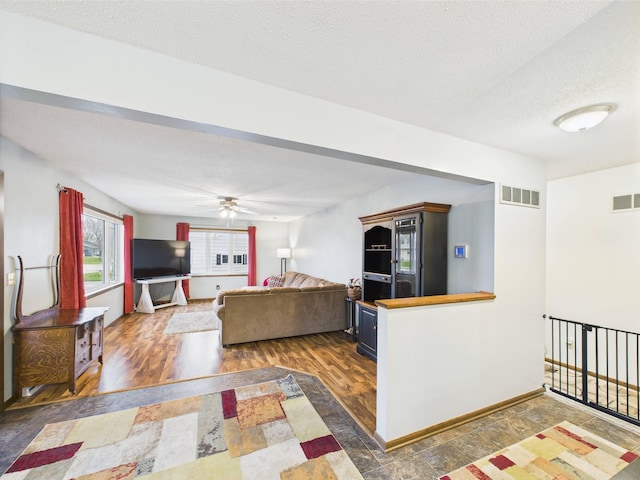 living room with baseboards, a textured ceiling, visible vents, and ceiling fan