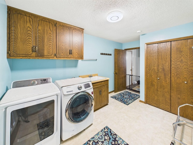clothes washing area featuring a textured ceiling, cabinet space, a sink, light floors, and separate washer and dryer