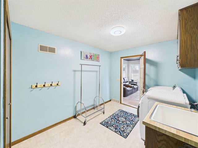 laundry area featuring washing machine and clothes dryer, cabinet space, a sink, a textured ceiling, and visible vents