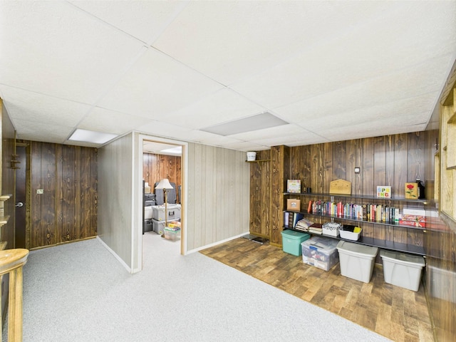 finished below grade area with baseboards, wood walls, carpet, and a drop ceiling