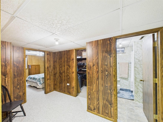 carpeted bedroom with connected bathroom, wood walls, and a drop ceiling