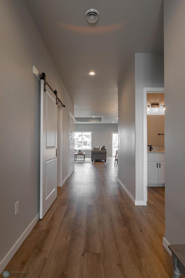 hall featuring visible vents, wood finished floors, a barn door, baseboards, and recessed lighting