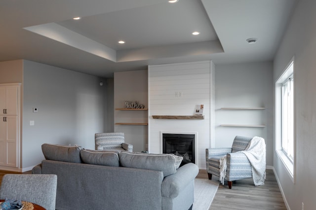 living room featuring a large fireplace, wood finished floors, baseboards, a tray ceiling, and recessed lighting