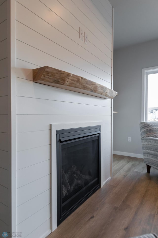 details featuring baseboards, a glass covered fireplace, and wood finished floors