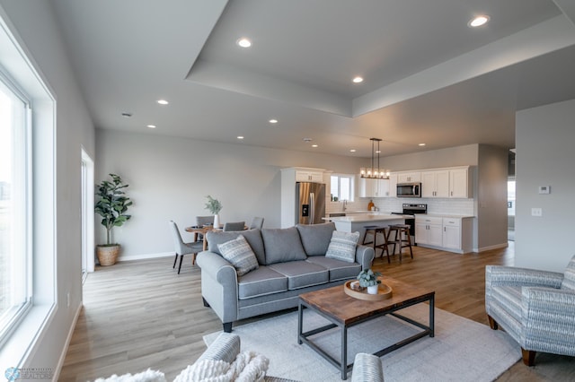 living room featuring recessed lighting, baseboards, light wood-type flooring, and a raised ceiling