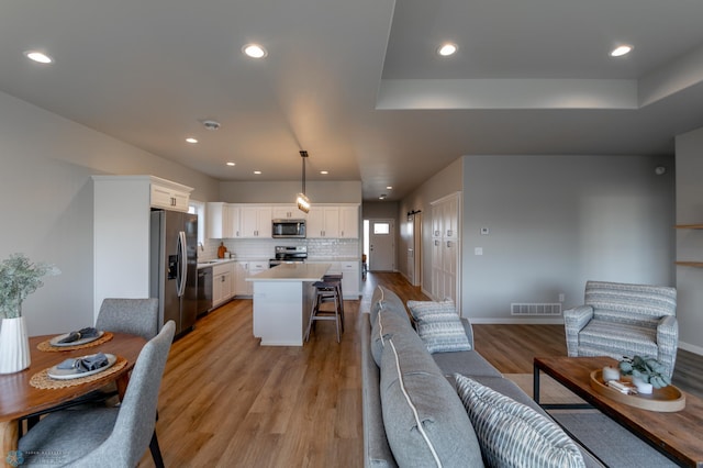living room with recessed lighting, a raised ceiling, baseboards, and light wood finished floors