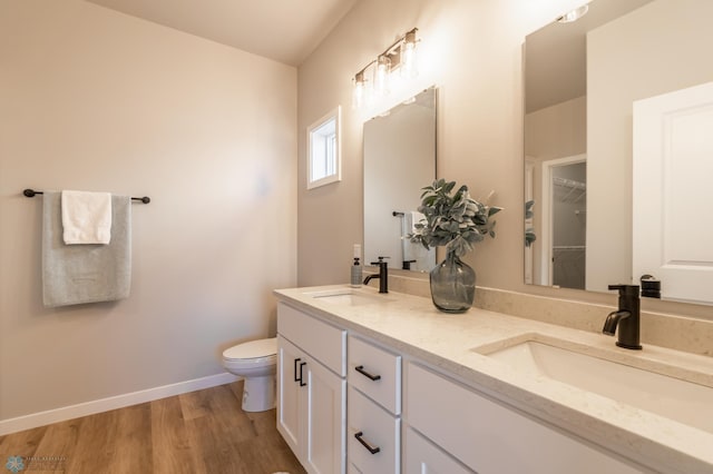 bathroom with a sink, double vanity, toilet, and wood finished floors
