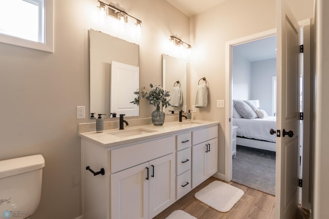 bathroom with a sink, double vanity, toilet, ensuite bathroom, and wood finished floors