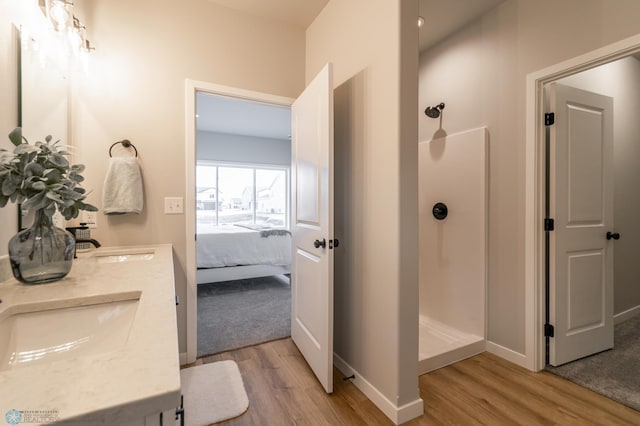 ensuite bathroom featuring a sink, a walk in shower, double vanity, and wood finished floors