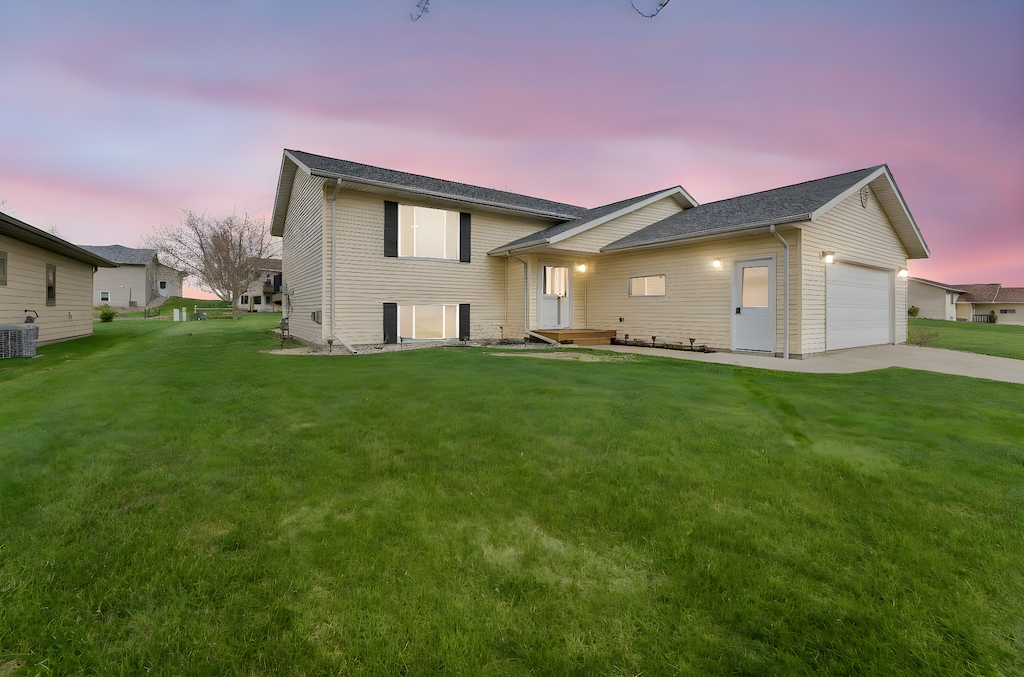 view of front facade featuring a lawn, central AC unit, an attached garage, and driveway