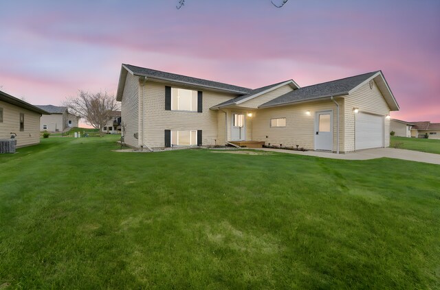 view of front facade featuring a lawn, central AC unit, an attached garage, and driveway