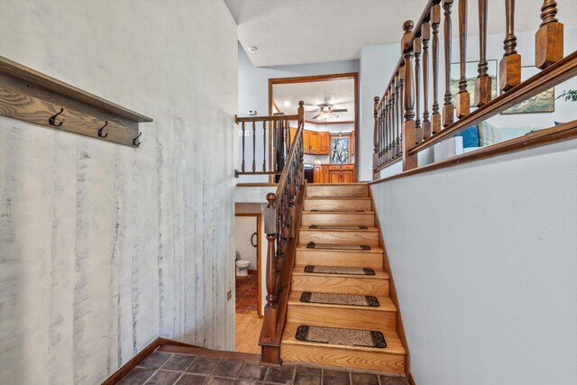 stairway with a ceiling fan and baseboards
