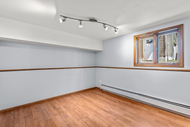spare room with a baseboard radiator, light wood-type flooring, baseboards, and rail lighting