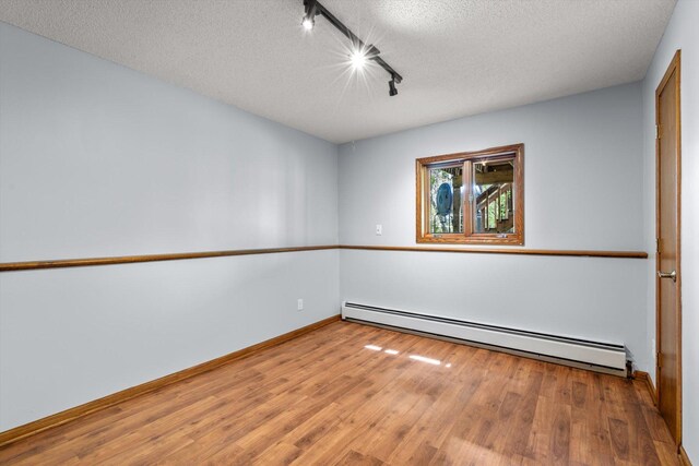 unfurnished room featuring a baseboard radiator, rail lighting, wood finished floors, and a textured ceiling