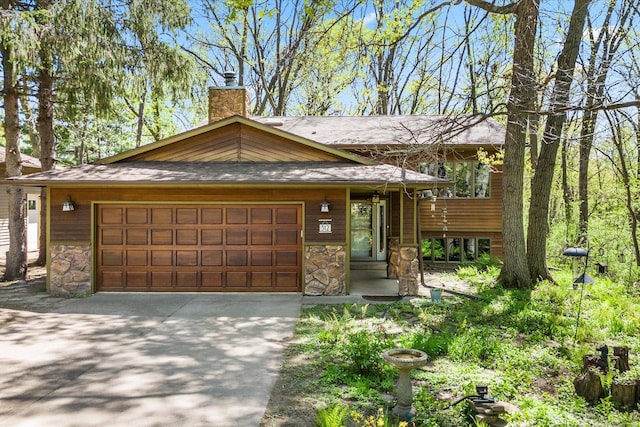 view of front of house featuring stone siding, driveway, a garage, and a chimney
