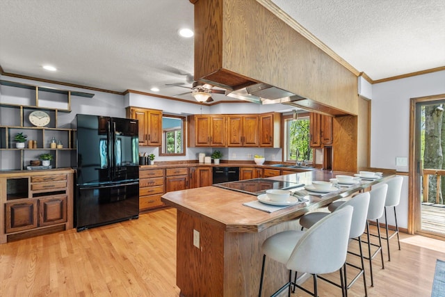 kitchen with black appliances, a textured ceiling, light wood-style flooring, brown cabinets, and ornamental molding