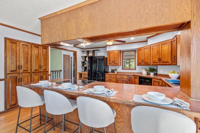 kitchen featuring black appliances, brown cabinetry, a peninsula, ornamental molding, and light wood finished floors