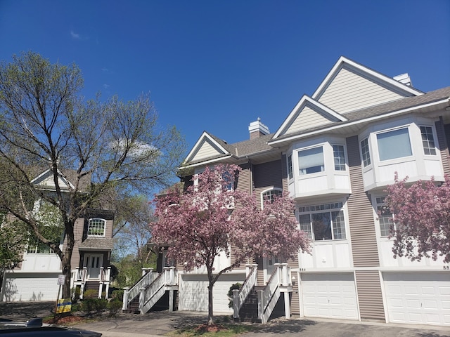 view of front of home featuring stairway, a garage, a chimney, and a shingled roof