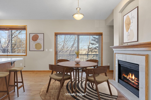 dining room featuring a tiled fireplace, light wood-style flooring, and baseboards