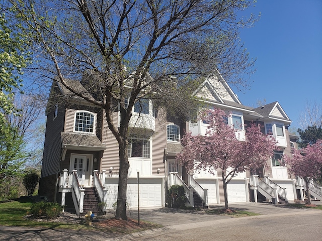 view of property with stairs, an attached garage, and driveway