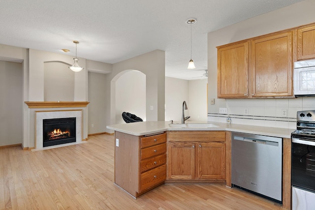 kitchen with stainless steel appliances, a sink, light wood-style flooring, light countertops, and decorative light fixtures