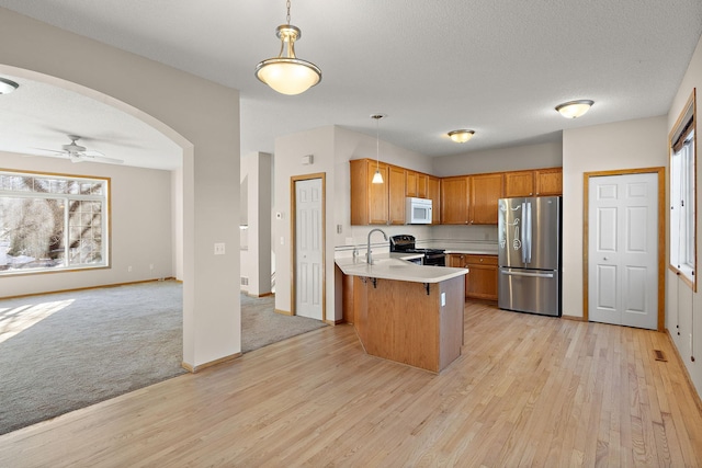 kitchen with appliances with stainless steel finishes, light countertops, a peninsula, light wood-type flooring, and pendant lighting
