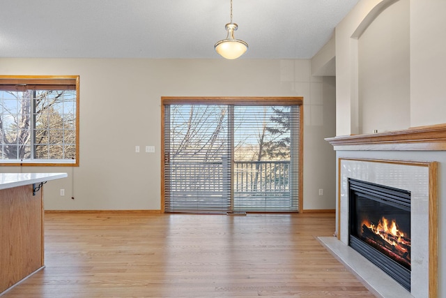 unfurnished living room featuring a tile fireplace, light wood-style floors, and baseboards