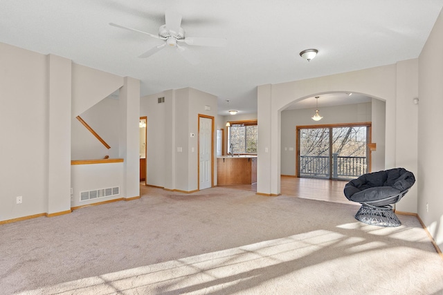 unfurnished living room with carpet floors, arched walkways, ceiling fan, and baseboards
