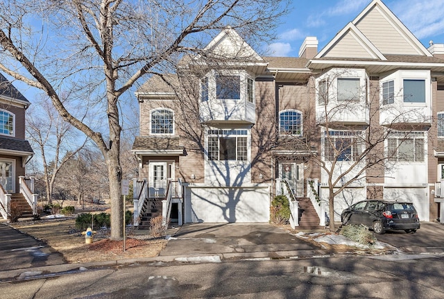 view of property featuring asphalt driveway, an attached garage, a chimney, and stairs