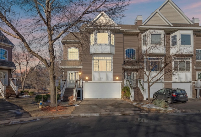 view of property with a garage, driveway, stairs, and a chimney