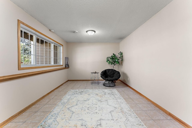 unfurnished room with a textured ceiling, light tile patterned floors, and baseboards