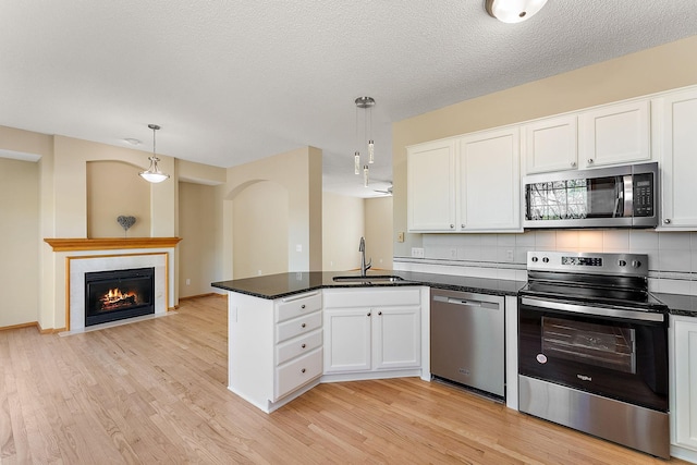 kitchen featuring stainless steel appliances, a sink, a peninsula, white cabinetry, and light wood-style flooring