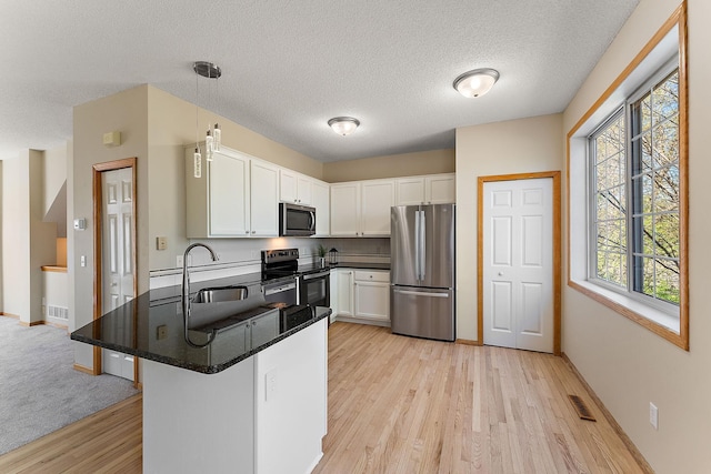 kitchen with stainless steel appliances, a sink, light wood-type flooring, white cabinets, and dark countertops