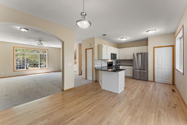 kitchen featuring stainless steel appliances, open floor plan, light wood-type flooring, dark countertops, and white cabinets