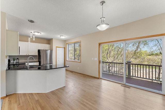 kitchen featuring freestanding refrigerator, a sink, light wood-style floors, dark countertops, and white cabinetry