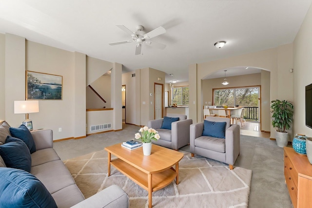 living area with light carpet, arched walkways, a ceiling fan, and baseboards
