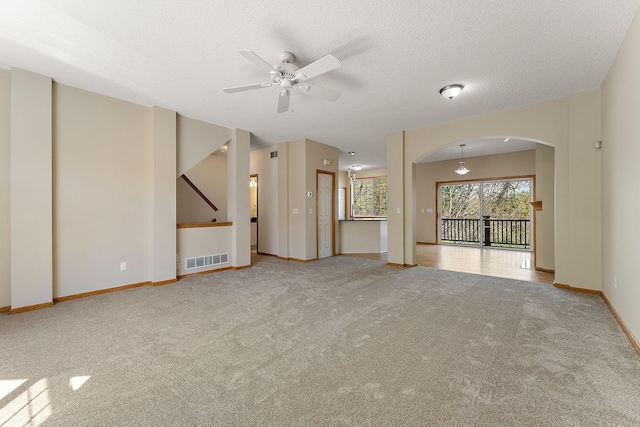 unfurnished living room featuring carpet floors, arched walkways, ceiling fan, baseboards, and a textured ceiling