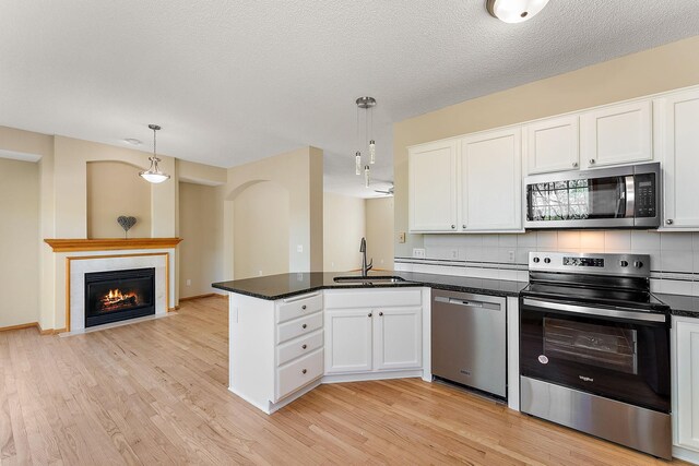 886 Trenton Ln N, Plymouth, MN 55441 - kitchen with appliances with stainless steel finishes, a sink, a peninsula, white cabinetry, and light wood-style flooring