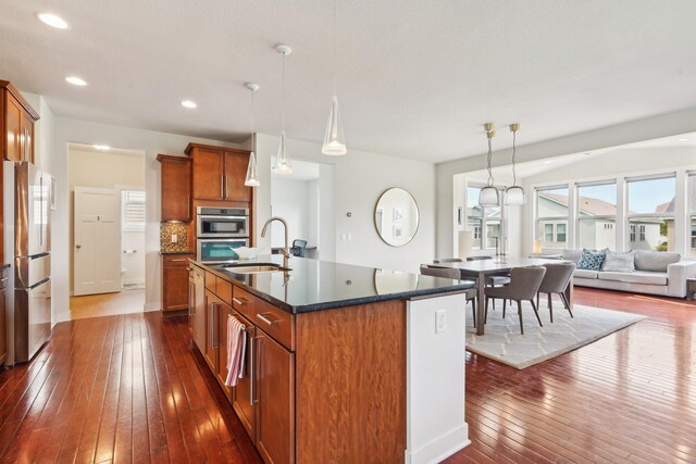 kitchen with stainless steel appliances, a sink, dark wood-style flooring, brown cabinetry, and recessed lighting