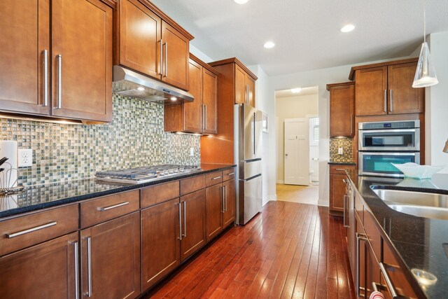 kitchen featuring under cabinet range hood, stainless steel appliances, dark stone counters, decorative backsplash, and recessed lighting