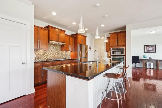 kitchen featuring appliances with stainless steel finishes, dark wood-type flooring, a sink, backsplash, and brown cabinets