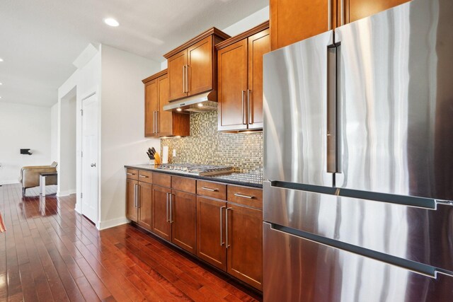 kitchen featuring stainless steel appliances, under cabinet range hood, brown cabinets, tasteful backsplash, and baseboards
