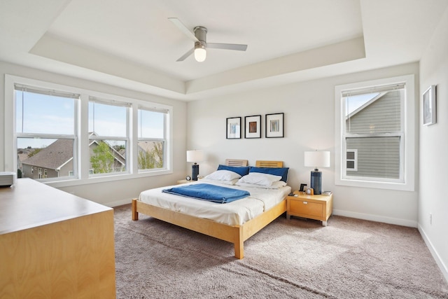 bedroom featuring a raised ceiling, carpet floors, baseboards, and a ceiling fan