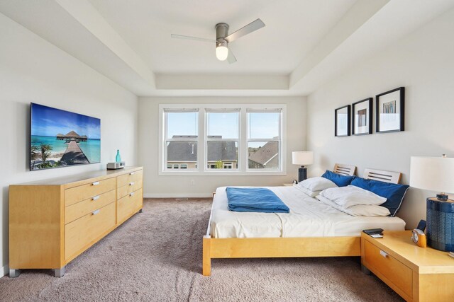 bedroom with a tray ceiling, light carpet, baseboards, and a ceiling fan