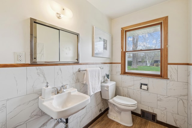 half bathroom featuring visible vents, wood finished floors, toilet, tile walls, and a sink