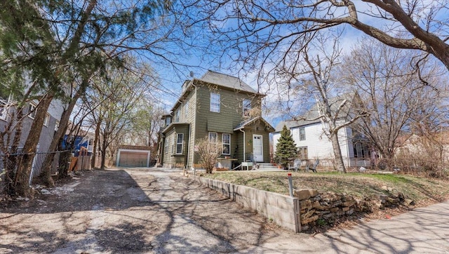 view of front facade with a detached garage, fence, an outbuilding, and aphalt driveway