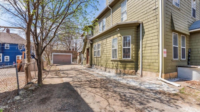 view of side of home with an outdoor structure, fence, driveway, and a detached garage