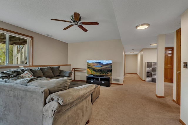 living area featuring a ceiling fan, light colored carpet, visible vents, and a textured ceiling